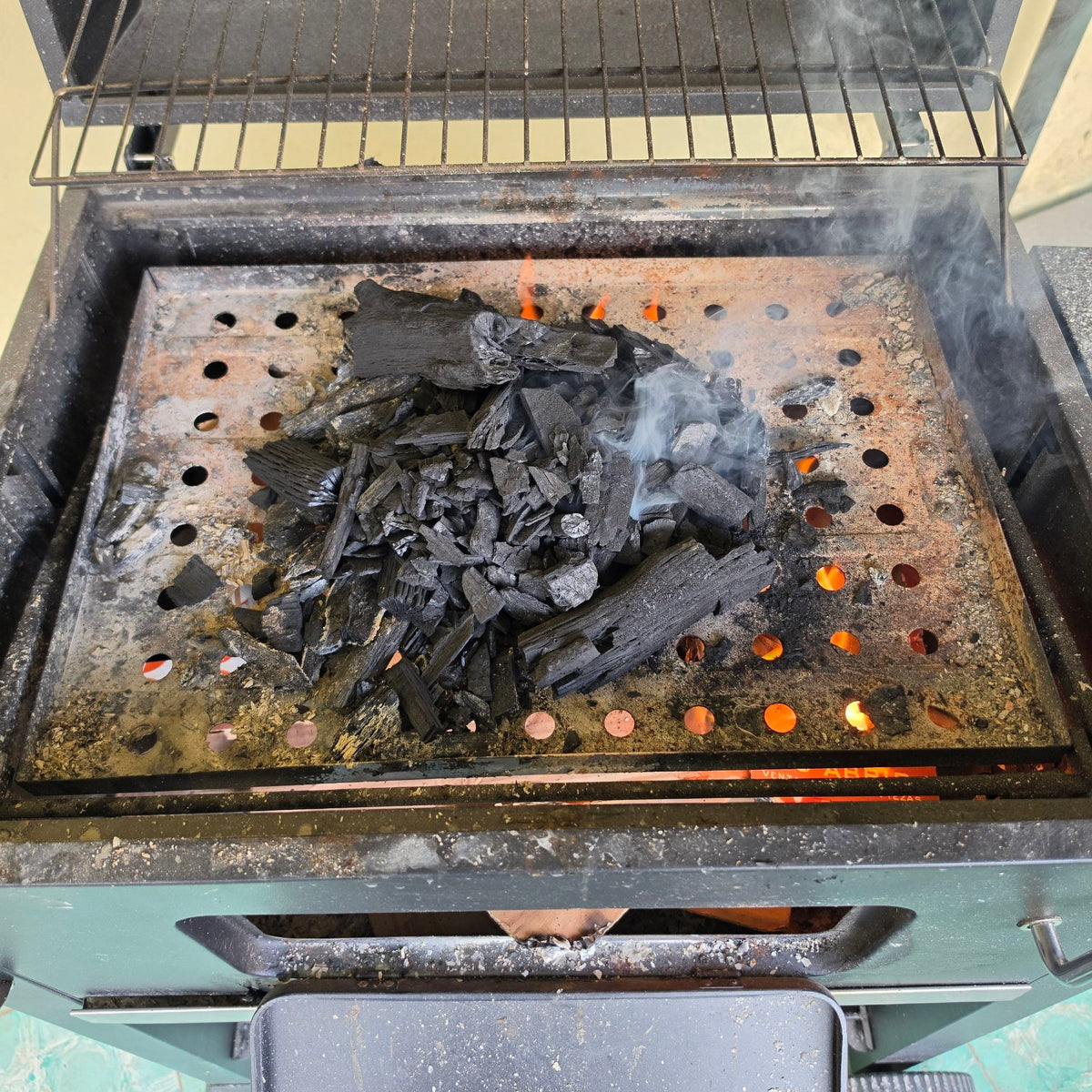 Carbón vegetal acomodado en la parrilla de carbón de un asador (asador no incluido)
