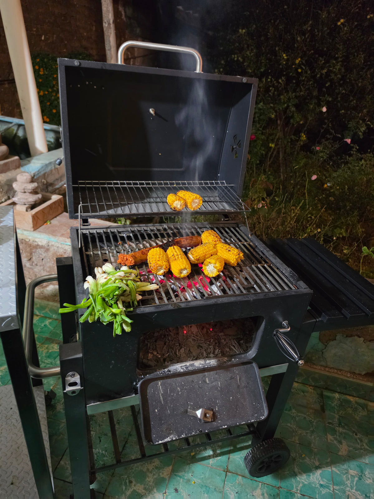 Asador de carbón Fiero de 24 pulgadas en uso, con brasas encendidas y elotes asados